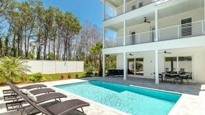 Une maison à deux étages avec une piscine, du mobilier d’extérieur et une vue sur les arbres.