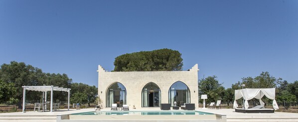 A pool area with a pergola, a covered seating area, and a building with arched windows. - Interior Designed "Mini Castle" with Pool in Puglia (Francavilla Fontana)