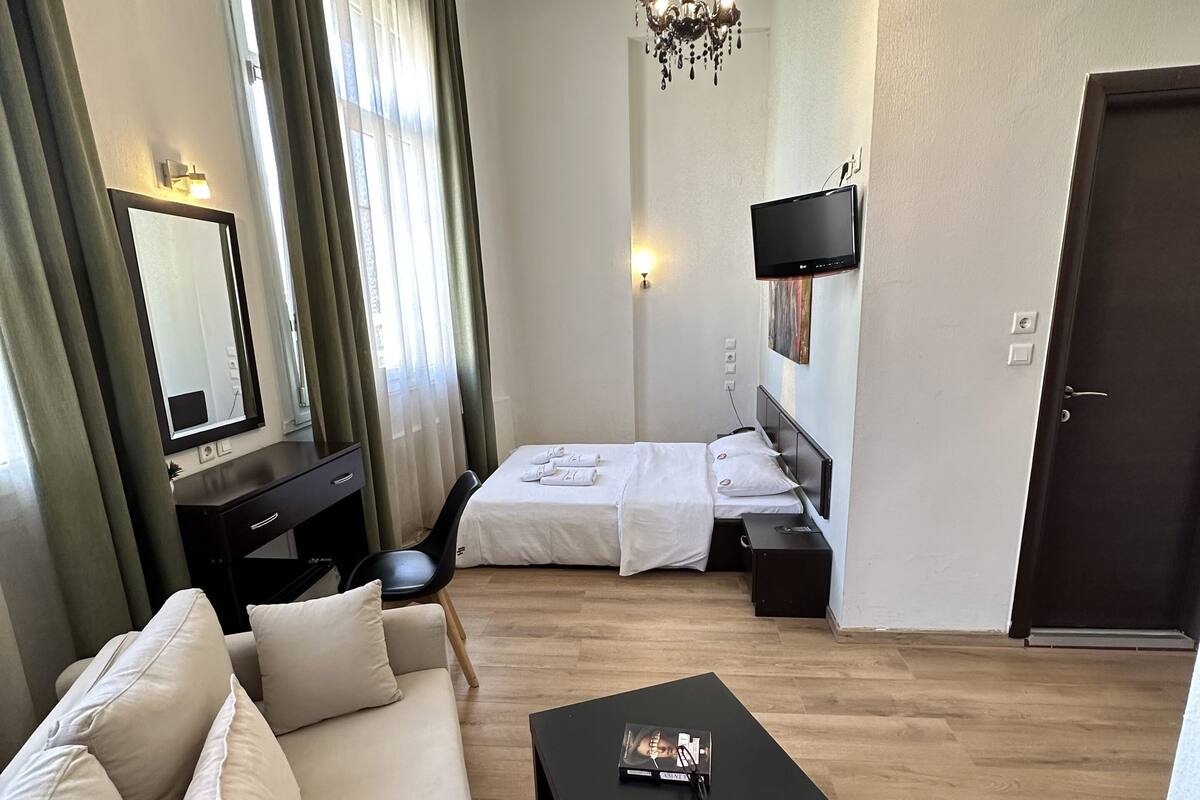 A hotel room with a sofa, a bed, a small table, a TV, and a chandelier.