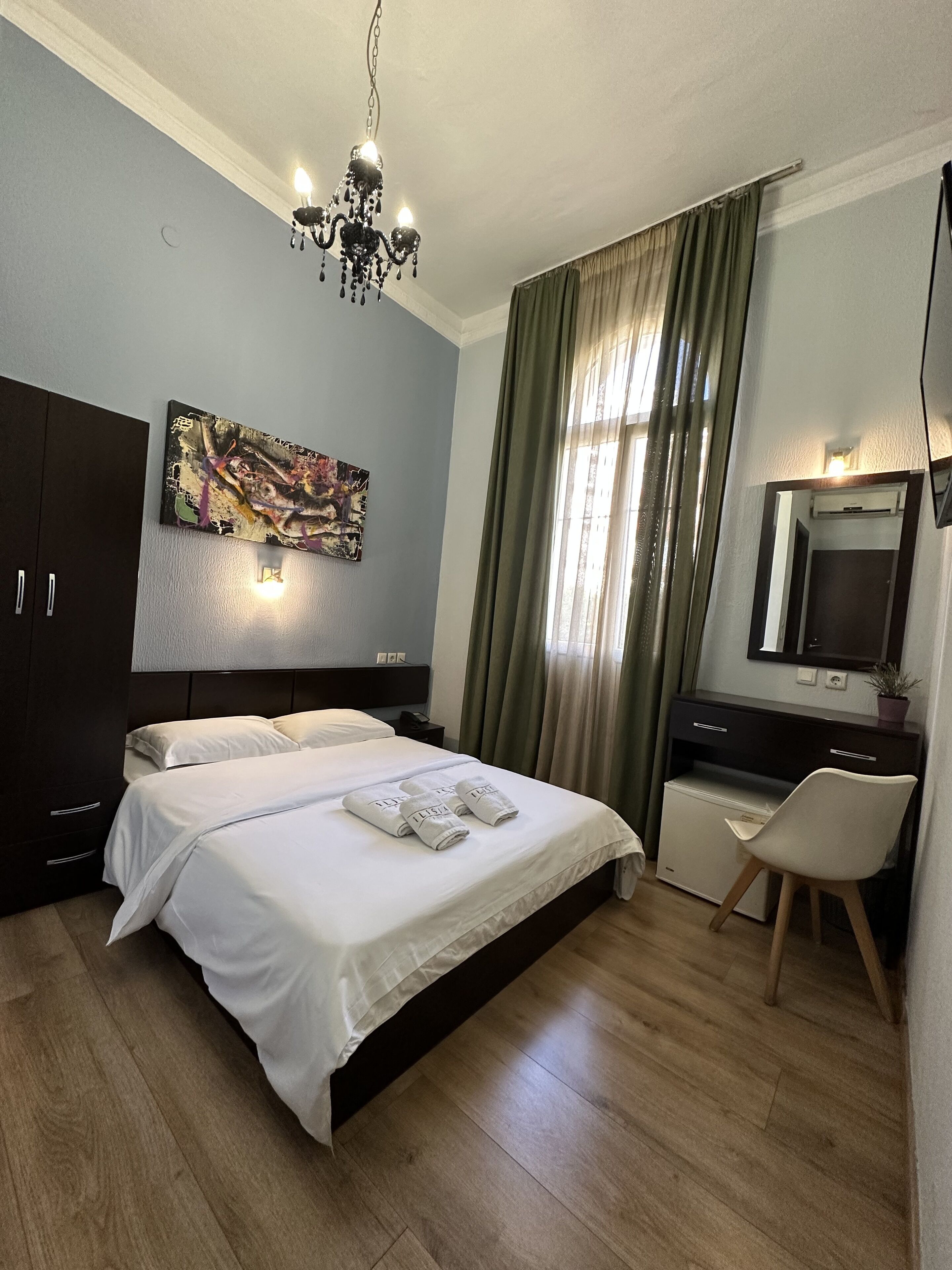 A modern hotel room with a large bed, a desk, a chair, a TV, and a painting on the wall.