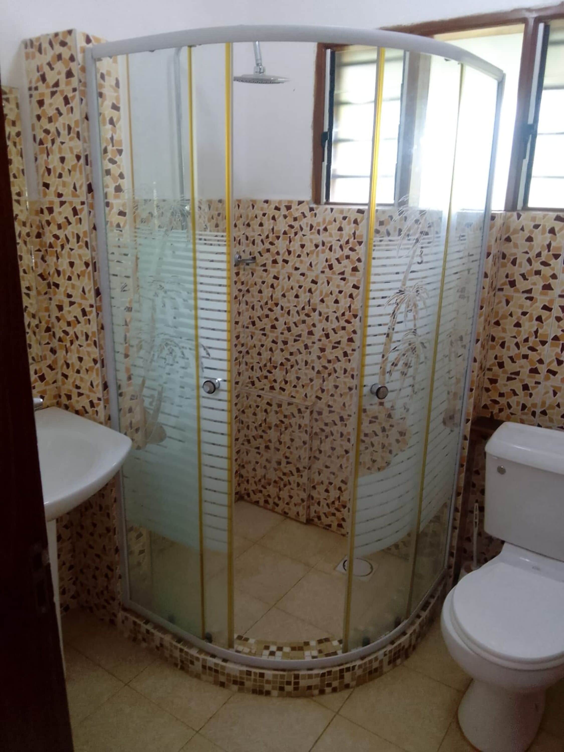 A bathroom with a glass-enclosed shower, a toilet, and a sink.
