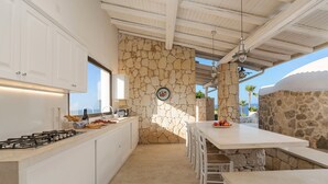 A modern kitchen with white cabinets, a stone accent wall, and a dining area with a stone table and chairs. - Villa with pool, sea front location , Plemmirio, DiCasaInSIcilia (Siracusa)