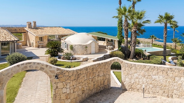A stone-walled property with a pool, palm trees, and a view of the sea. - Villa with pool, sea front location , Plemmirio, DiCasaInSIcilia (Siracusa)
