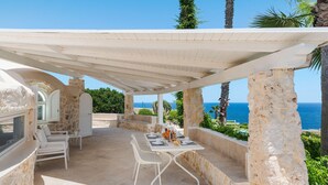 A covered outdoor dining area with a table and chairs, stone walls, and a view of the sea. - Villa with pool, sea front location , Plemmirio, DiCasaInSIcilia (Siracusa)