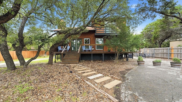 Une cabane en bois dotée d’une terrasse, de meubles de jardin et d’un chemin de gravier menant à l’entrée.