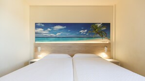 A bedroom with a bed centered under a beach scene painting, two bedside tables with lamps, and a wooden headboard. - FESTIVAL VILLAGE APARTMENTS (Salou)