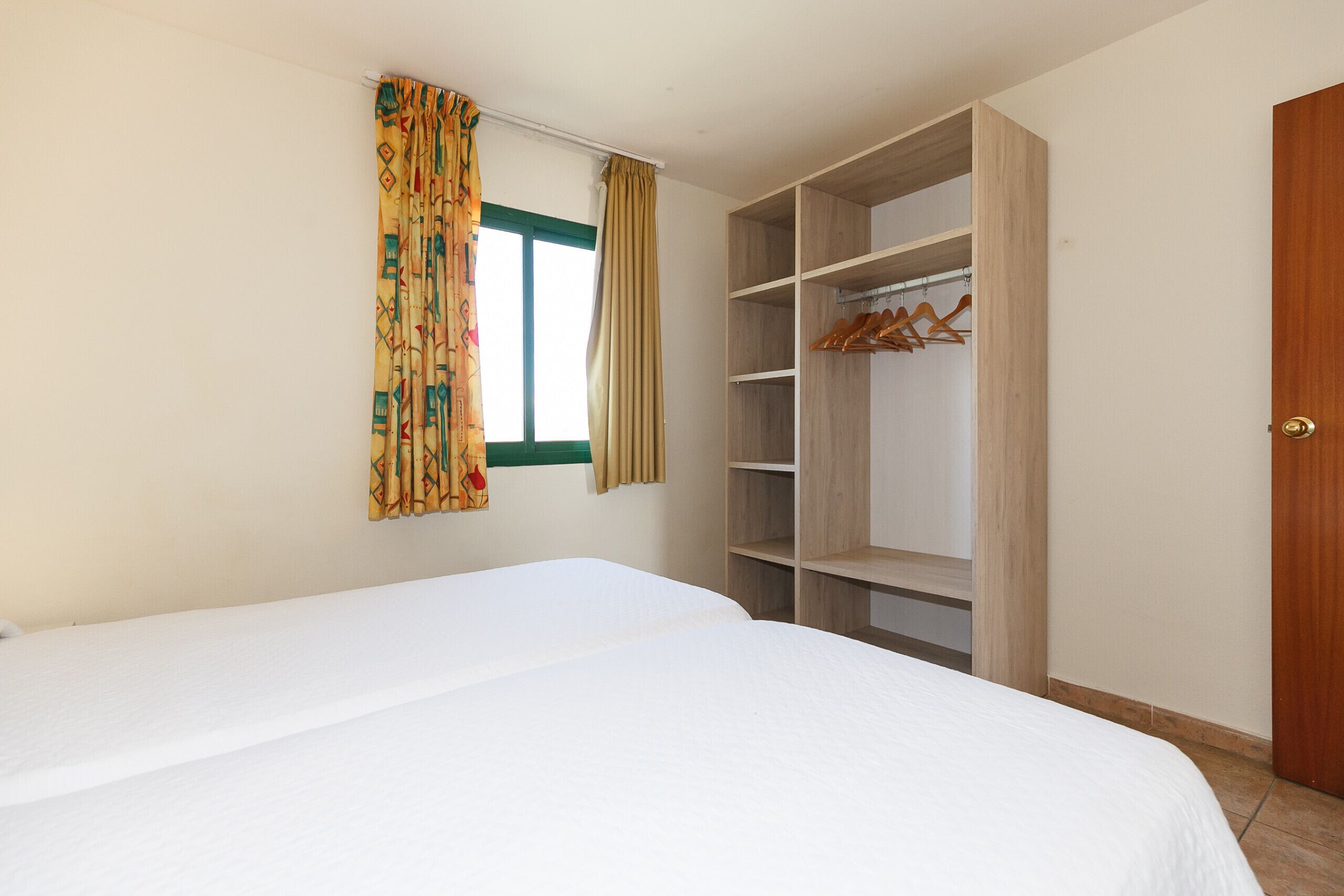 A bedroom with a bed, a wardrobe with multiple shelves, and a window with curtains.