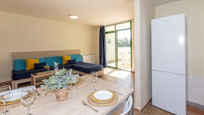 A modern living room with a sofa, a dining table set for two, and a white refrigerator. - FESTIVAL VILLAGE APARTMENTS (Salou)