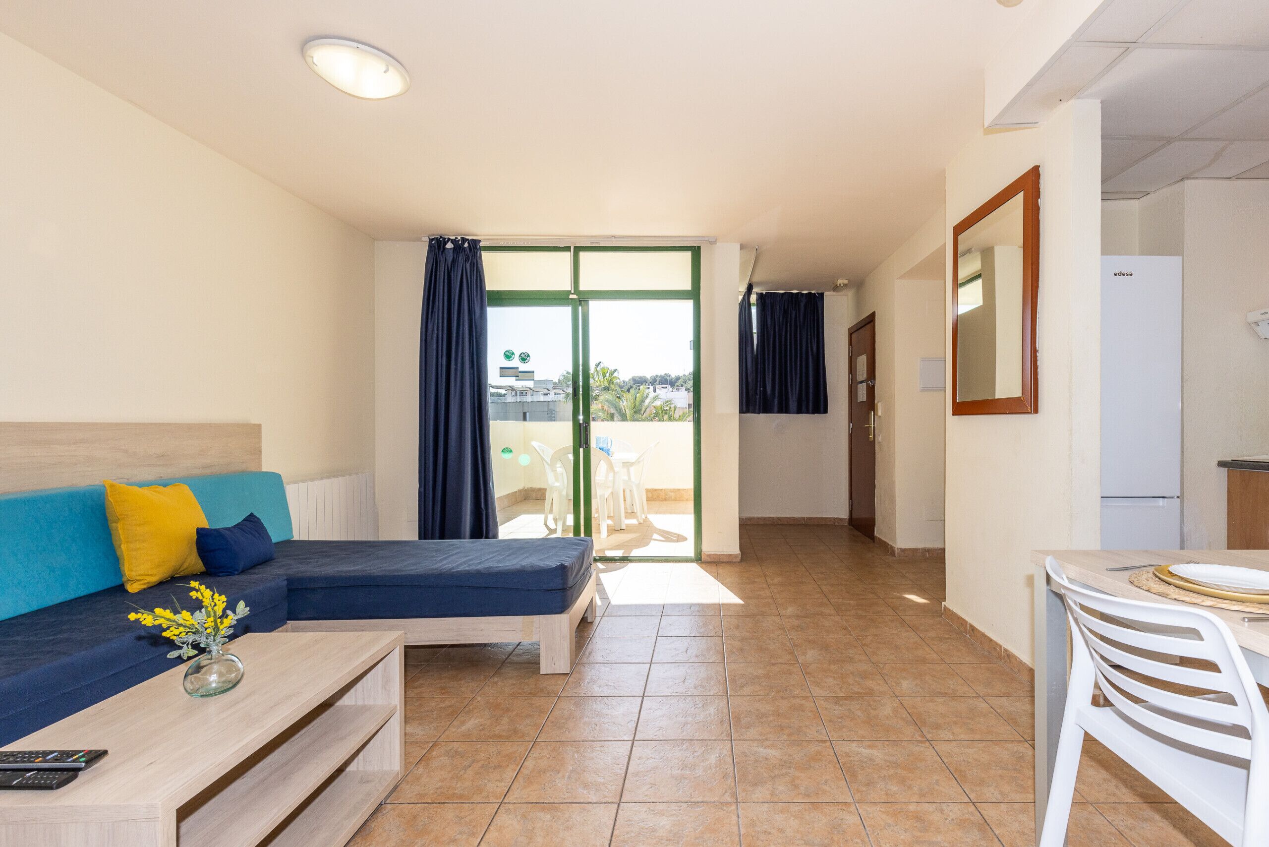 A room with a bed, a sofa, a dining table, and a view through a glass door.