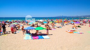 En välbesökt strand med många färgglada parasoller och folk som solar.