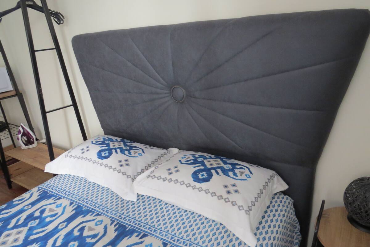 A bed with a grey upholstered headboard, patterned pillows, and a blue and white bedspread.