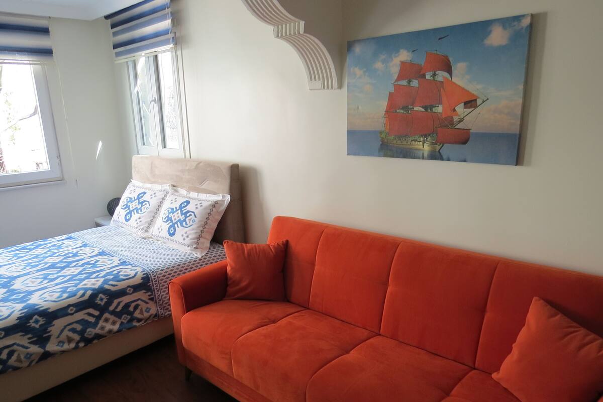 A bedroom with a bed, a sofa, a window, and a painting on the wall.