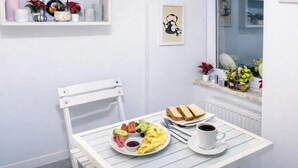 Ein Frühstückstisch mit Toast, Eiern und Kaffee, vor einer weißen Wand mit Fenster und Ablage mit Dekoration.