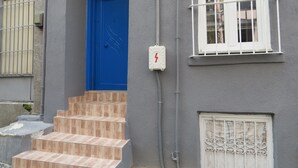 Ein Gebäude mit einer blauen Tür, einem Fenster mit weißen Gitterstäben und einer Treppe, die zum Eingang führt.