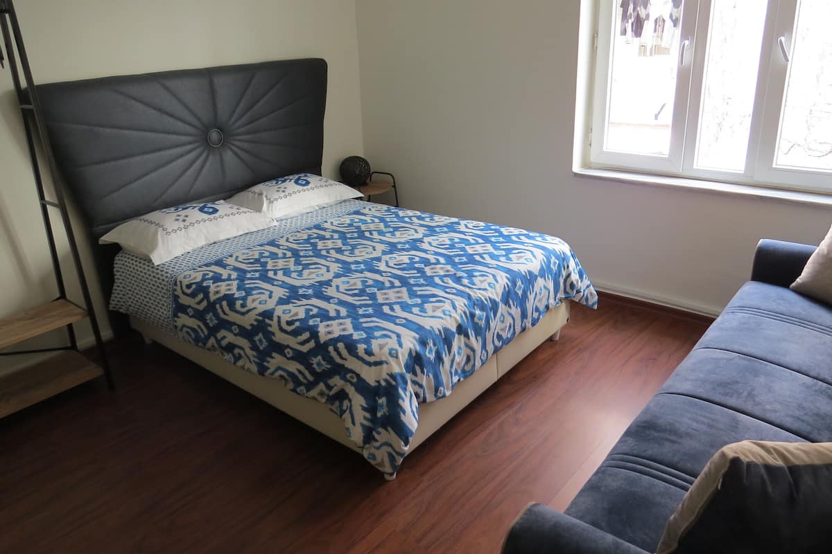 A bedroom with a bed, a window, a sofa, and a wooden floor.