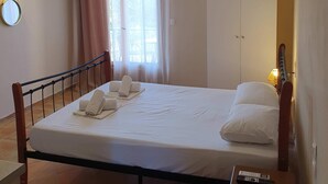 A neatly made bed with white linens and towels, a bedside table with a remote control, a television mounted on the wall, and a wardrobe. - Georgias House Project Ground Floor (Skiathos)