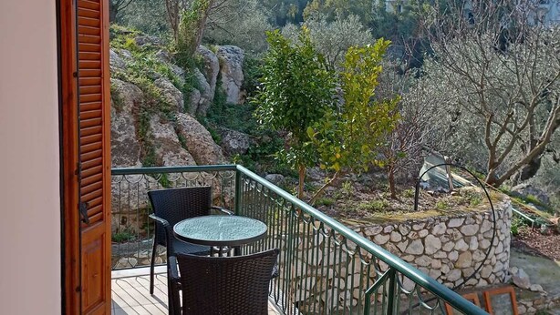 A balcony with a table and chairs, overlooking a mountainous landscape with trees and buildings. - Georgias House Project Ground Floor (Skiathos)