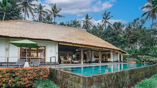 Ein Resort mit Pool, einem strohgedeckten Gebäude und üppiger tropischer Landschaft.