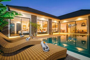 Una casa moderna con piscina, sillones de mimbre y un interior bien iluminado.