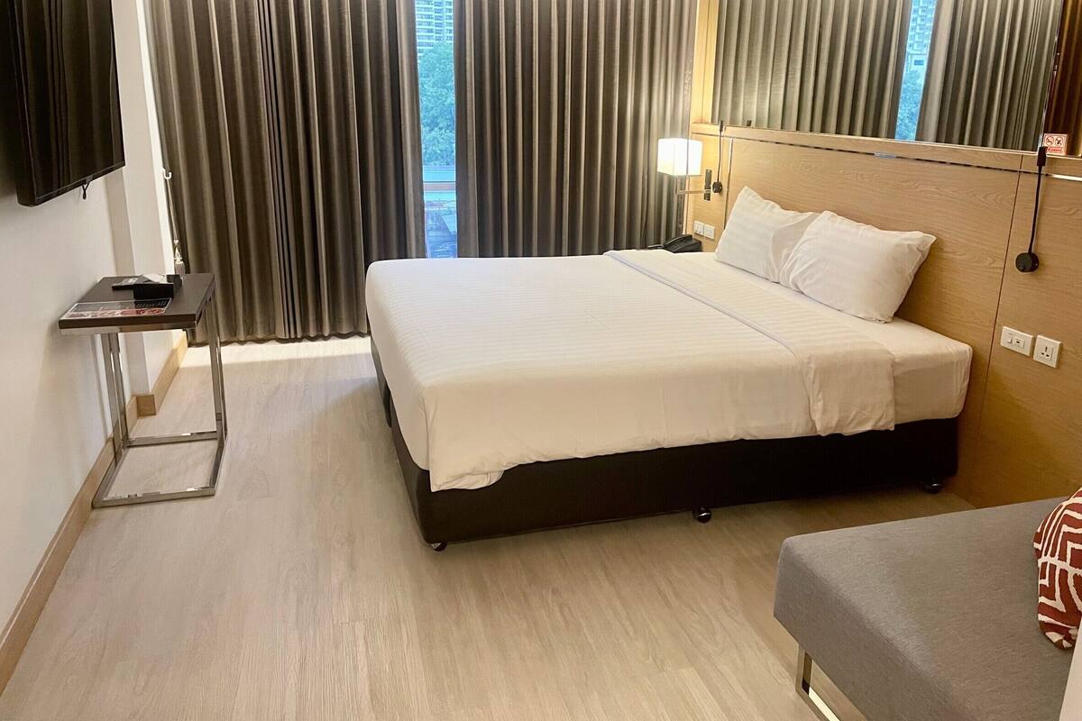 Una habitación de hotel con cama, mesita de noche, lámpara y vistas por la ventana.