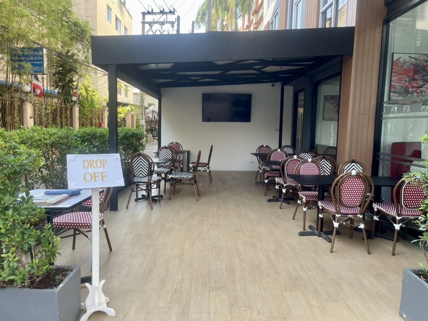 An outdoor seating area with tables and chairs, a 'DROP OFF' sign, and a building in the background.