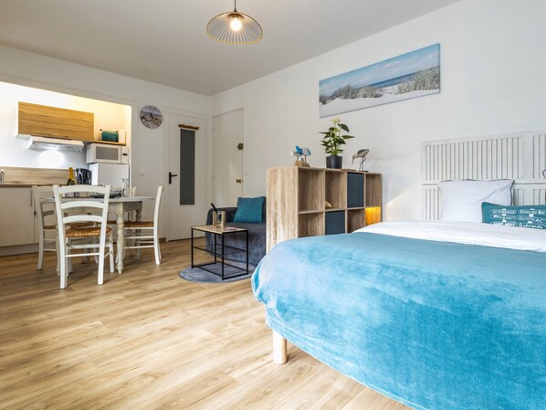 Ein Schlafzimmer mit Bett, Schreibtisch und Stuhl. Es gibt ein Fenster mit Vorhängen, eine Pflanze auf dem Schreibtisch und ein Bild an der Wand.