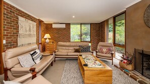 Een woonkamer met een bakstenen muur, leren banken, een houten salontafel en een open haard.