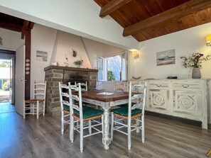 Un comedor con mesa de madera y sillas blancas, chimenea de piedra y un armario blanco.