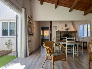 Um interior aconchegante com área de jantar, cadeiras de vime, estante de livros e lareira de pedra.