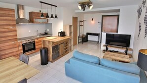 A modern kitchen with a central island, a dining area with a wooden table, and a living room with a blue sofa and a TV.