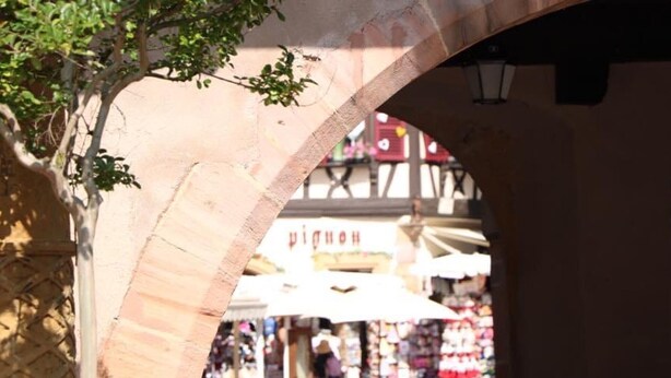 An outdoor café area with tables and chairs under a stone archway.