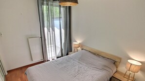 A bedroom with a large bed, two bedside lamps, a radiator, and a window with curtains.