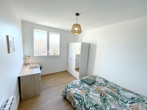 A bedroom with a bed, a desk, a wardrobe, and a window.