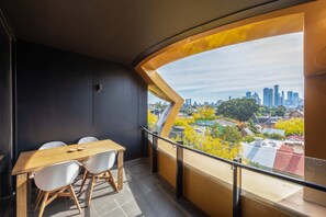 A modern balcony with a curved glass railing, a wooden table, and white chairs. - 2-bed in South Melbourne w/ Beautiful City Views (South Melbourne)