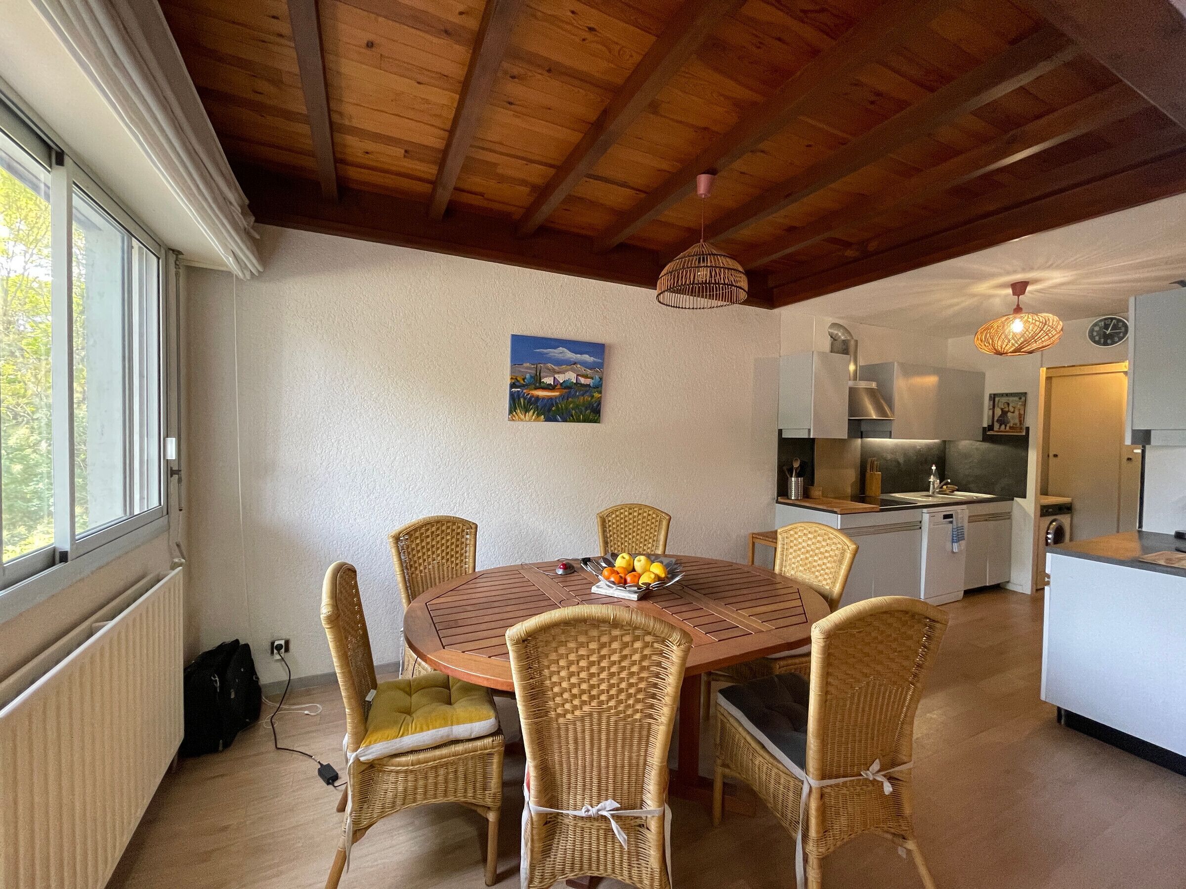 A dining area with a round table, wicker chairs, and a fruit bowl.