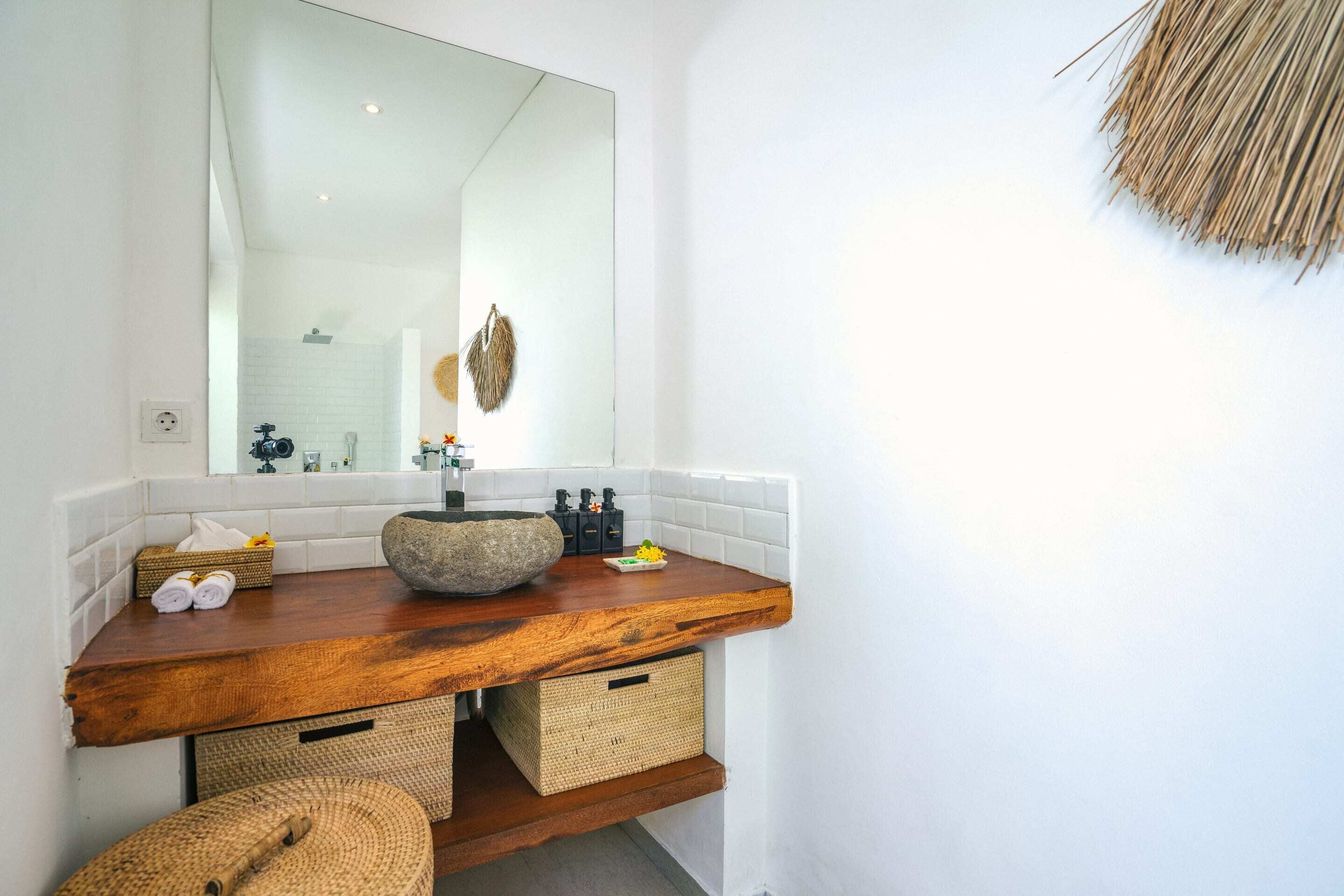 Une salle de bain avec un meuble-lavabo en bois, un grand miroir et un lavabo en pierre.