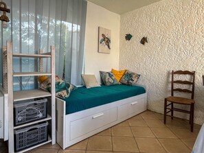 A bedroom with a bed, a chair, a shelf unit, and a wall with textured plaster.