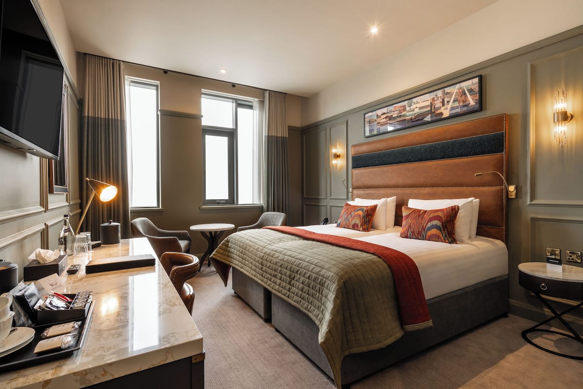Une chambre d’hôtel avec un grand lit, un bureau avec une lampe, une chaise et une petite table.