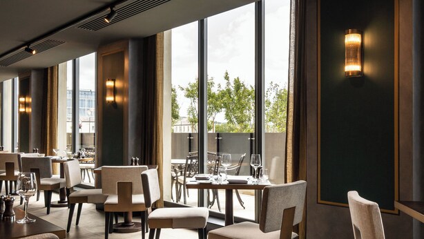 Un interior de restaurante moderno con techos altos, ventanas amplias y una fila de mesas y sillas.