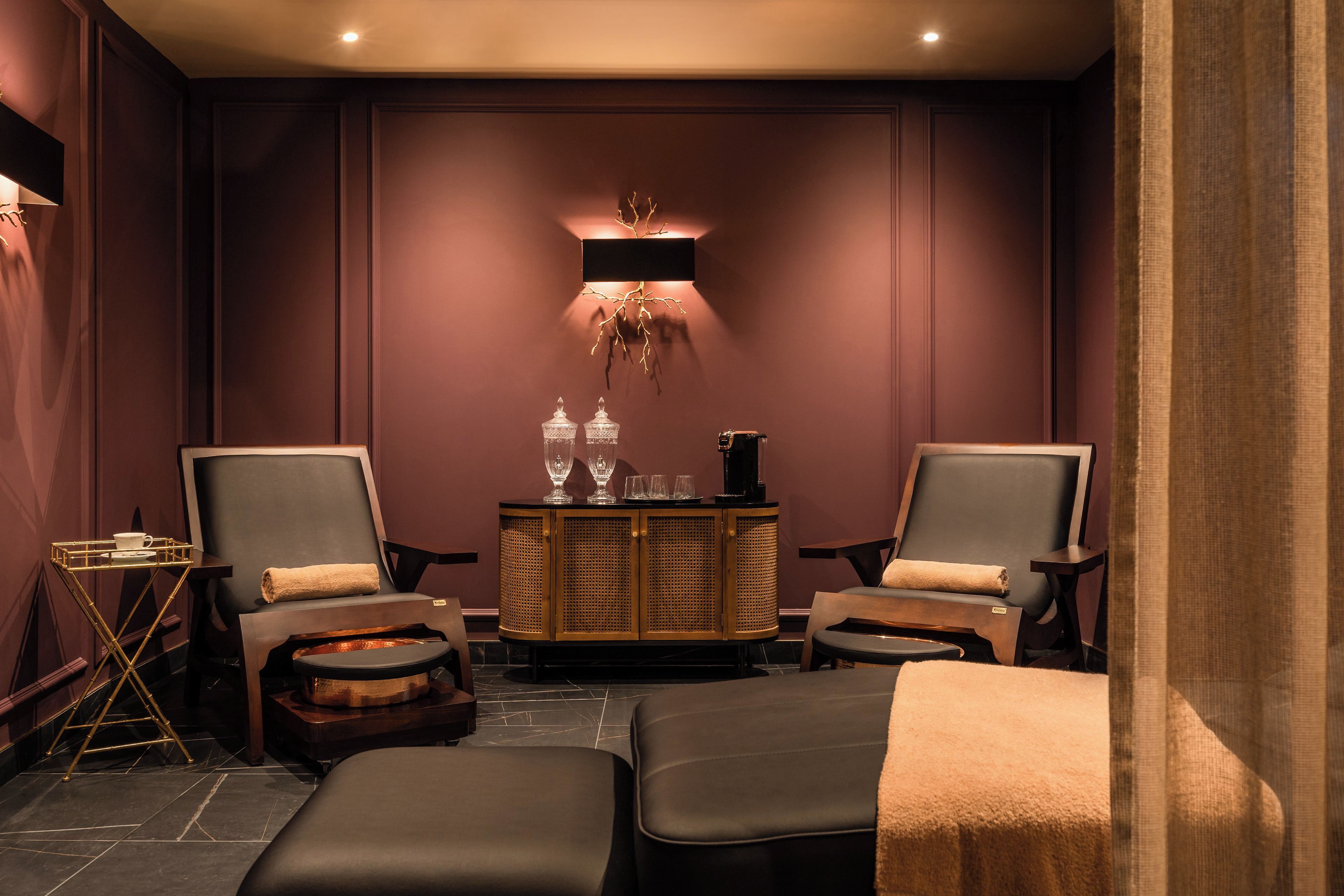 A spa room with two massage chairs, a wooden cabinet with glassware, and a small table with a tray.