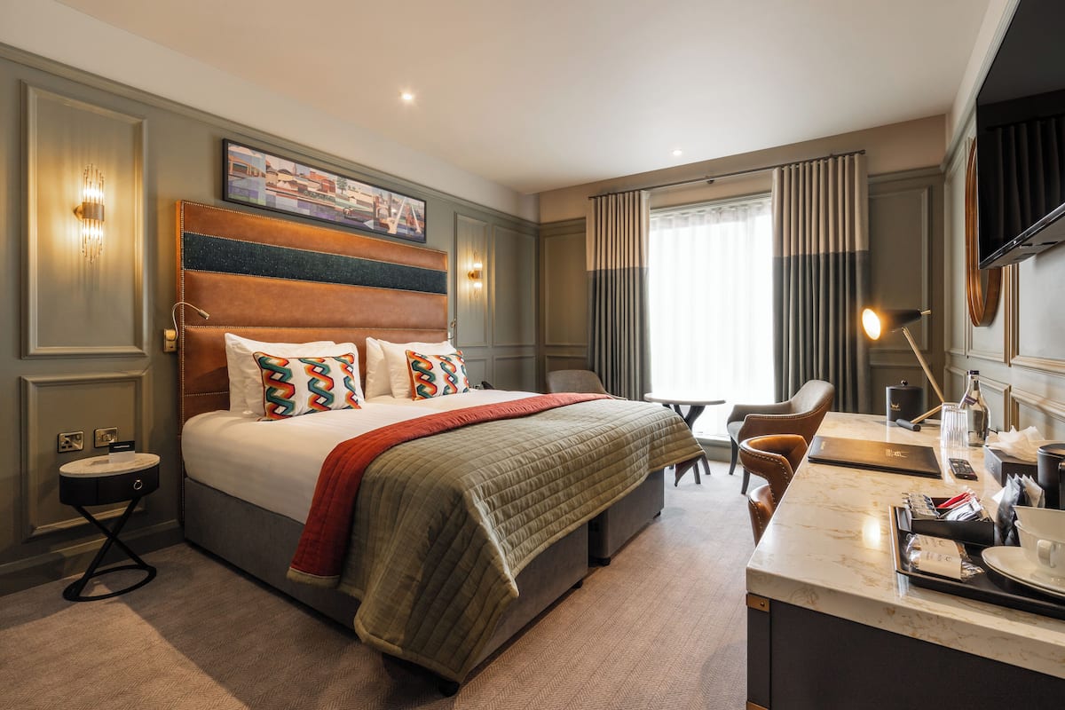 Une chambre d’hôtel avec un grand lit, un bureau avec une chaise, une table de chevet et une fenêtre avec des rideaux.