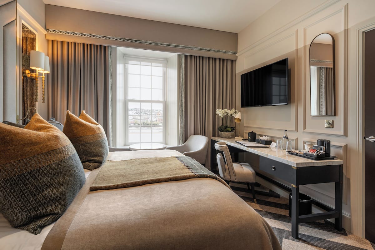Une chambre d’hôtel avec un grand lit, un bureau, une chaise, une télévision et une fenêtre avec des rideaux.