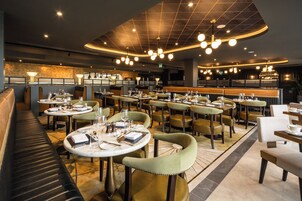 Un restaurante con mesas redondas, sillas tapizadas en verde y una zona de bar.