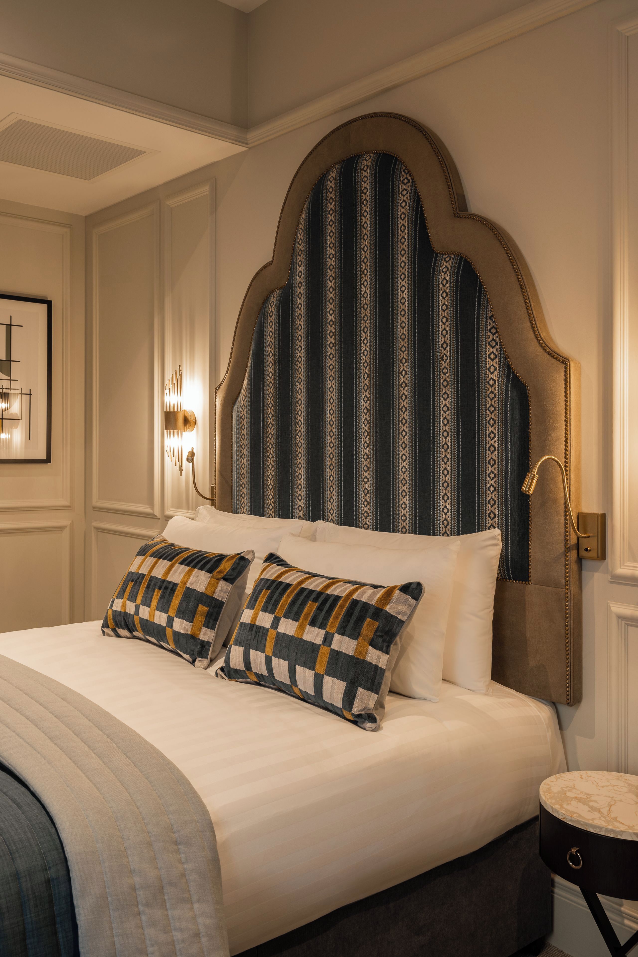 A neatly made bed with a patterned headboard, a bedside lamp, and a framed picture on the wall.