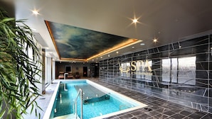 Una piscina interior moderna con vistas despejadas al techo y a las paredes, una zona de estar y un amplio ventanal.