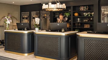 Una zona de recepción con tres mostradores, una araña y una estantería con objetos decorativos.