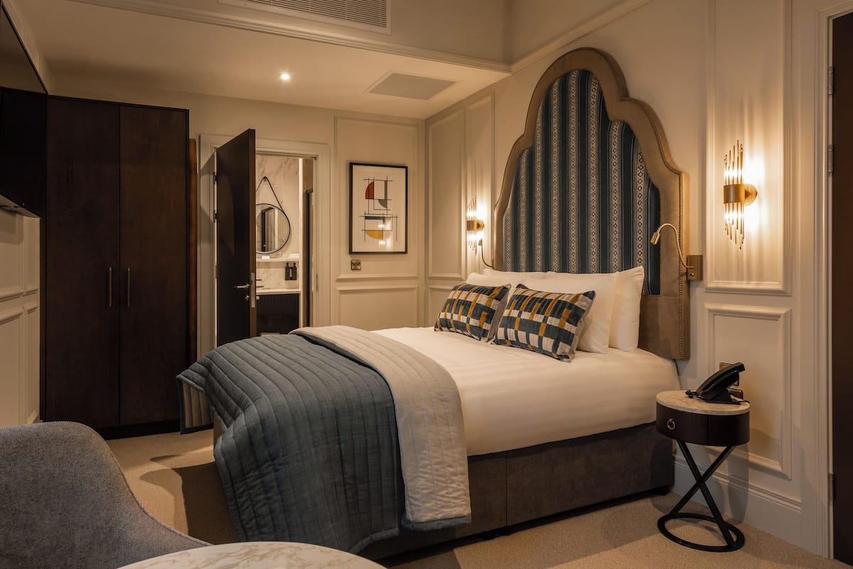 Une chambre à coucher bien rangée, avec un grand lit, une table de chevet avec un téléphone, une armoire et un tableau encadré au mur.