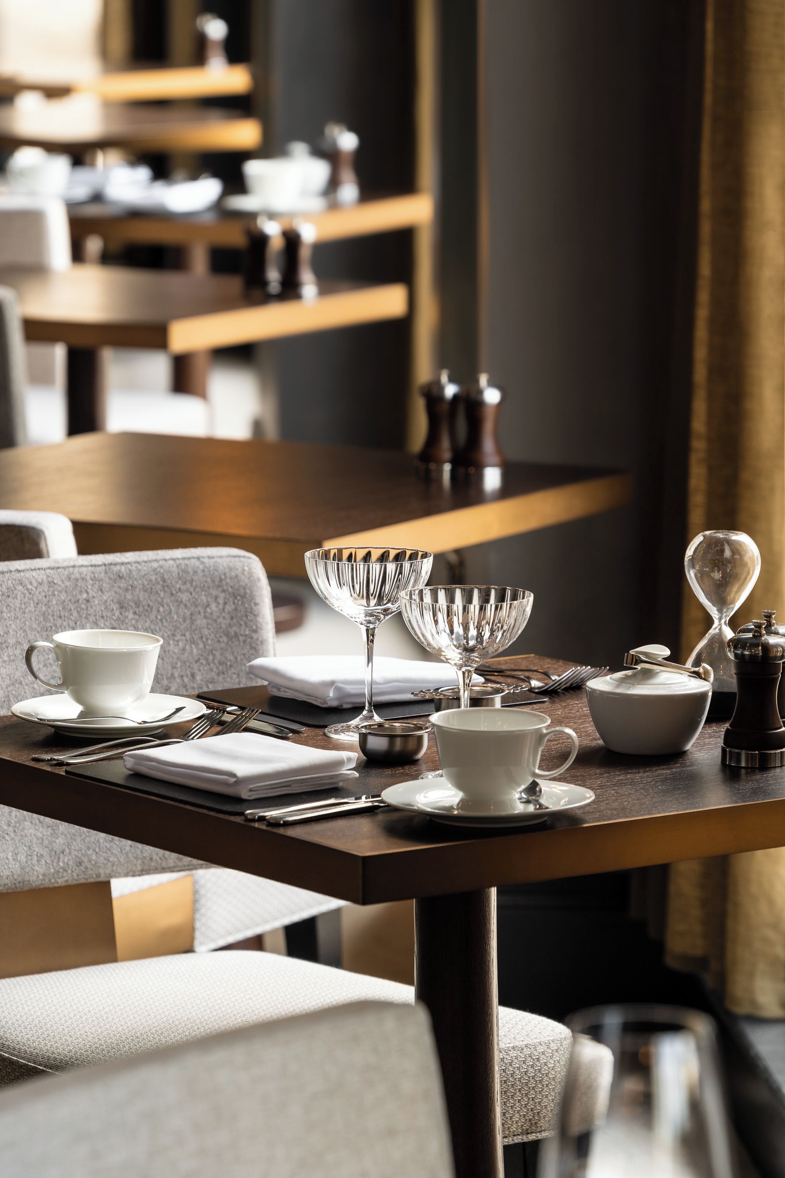 A dining table set with white cups, saucers, a glass, and a pepper grinder.