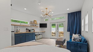 Ein modernes Schlafzimmer mit einem großen Bett, einem blauen Sofa, einem kleinen Tisch und einer Küchenzeile mit Fernseher.