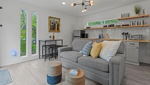 Eine moderne Küche mit weißen Schränken, einem Einbauofen und einer Mikrowelle. Es gibt eine Essecke mit Tisch und Stühlen sowie ein graues Sofa mit Kissen.